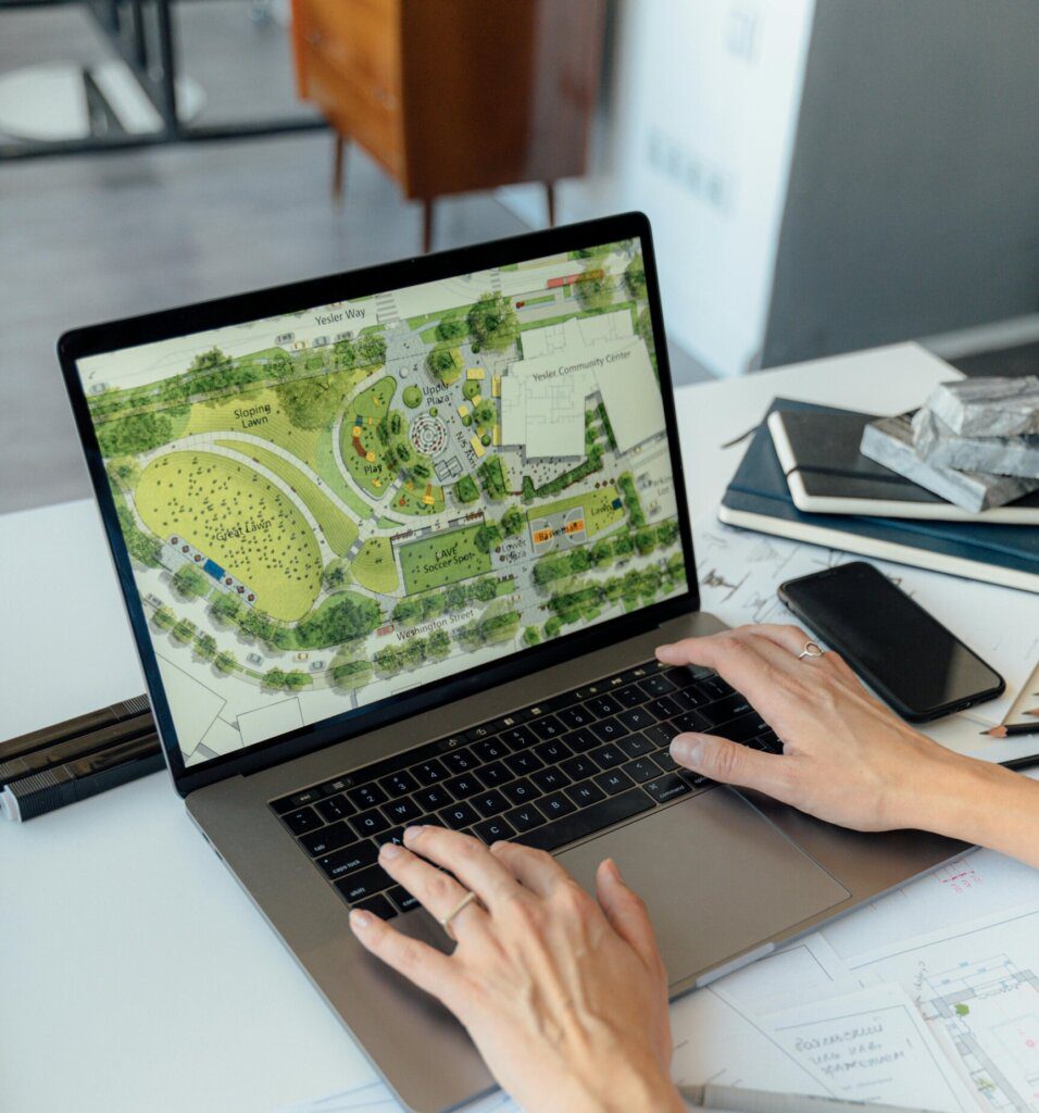 Architect working on landscape plan displayed on laptop with hands typing on keyboard.